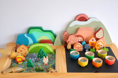 Colorful toy landscape with mountains, houses, and animals on a wooden base.