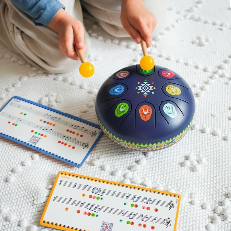Child playing with a colorful drum toy on a textured surface with music sheets nearby.