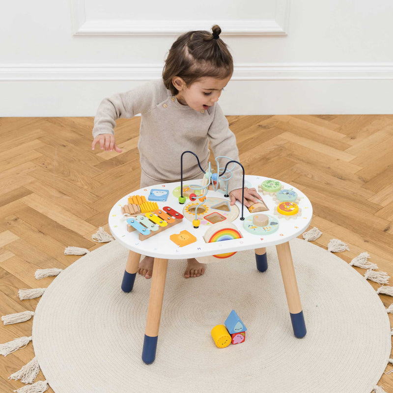 Child playing with a colorful educational toy table on a wooden floor.