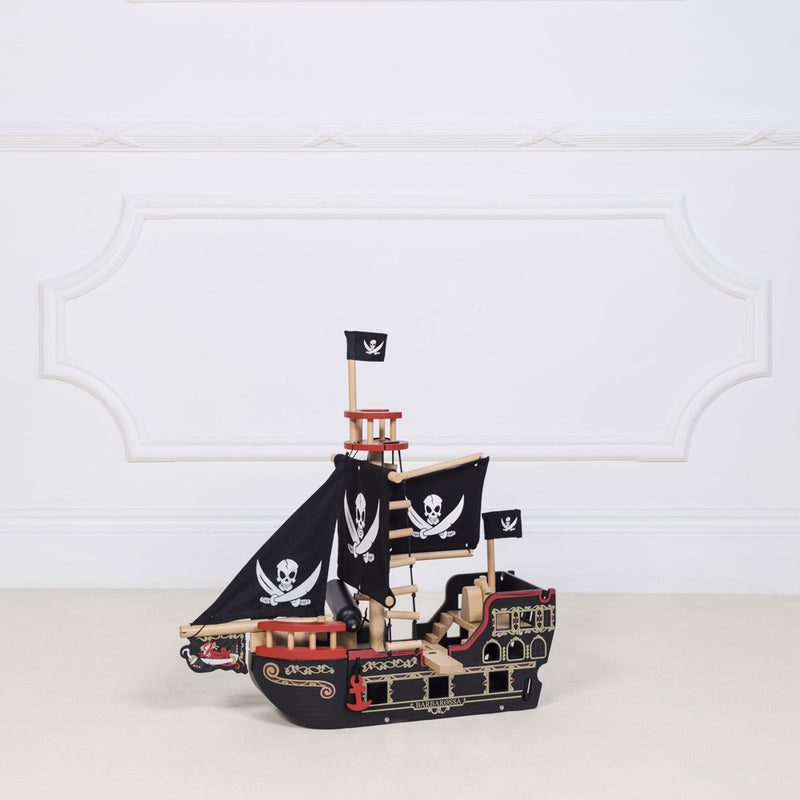 Wooden pirate ship model with flags on a white surface and light gray background