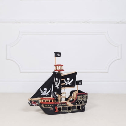 Wooden pirate ship model with flags on a white surface and light gray background