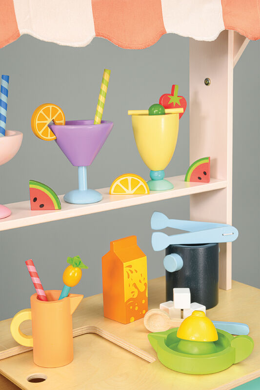 Colorful toy kitchen set with drinks and utensils on a wooden shelf against a gray background.