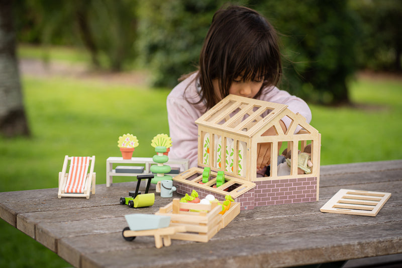 Child playing with a wooden toy garden set on a table outdoors.