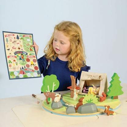 Child playing with a wooden playset featuring animals and trees, holding a map.
