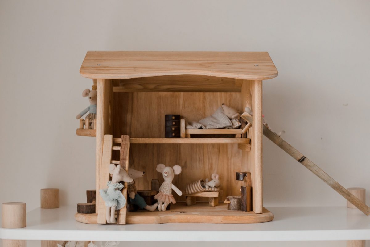 Wooden dollhouse with miniature furniture and dolls on a white surface.