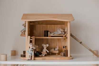 Wooden dollhouse with miniature furniture and dolls on a white surface.