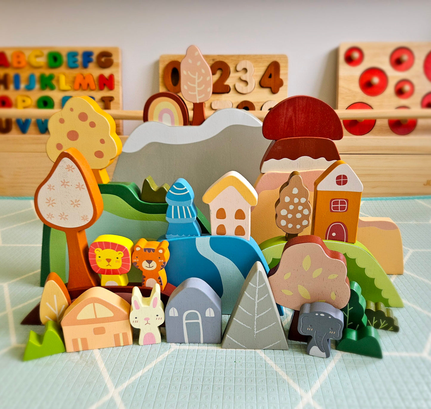 Set of wooden toys including houses, animals, and a landscape on a checkered surface.
